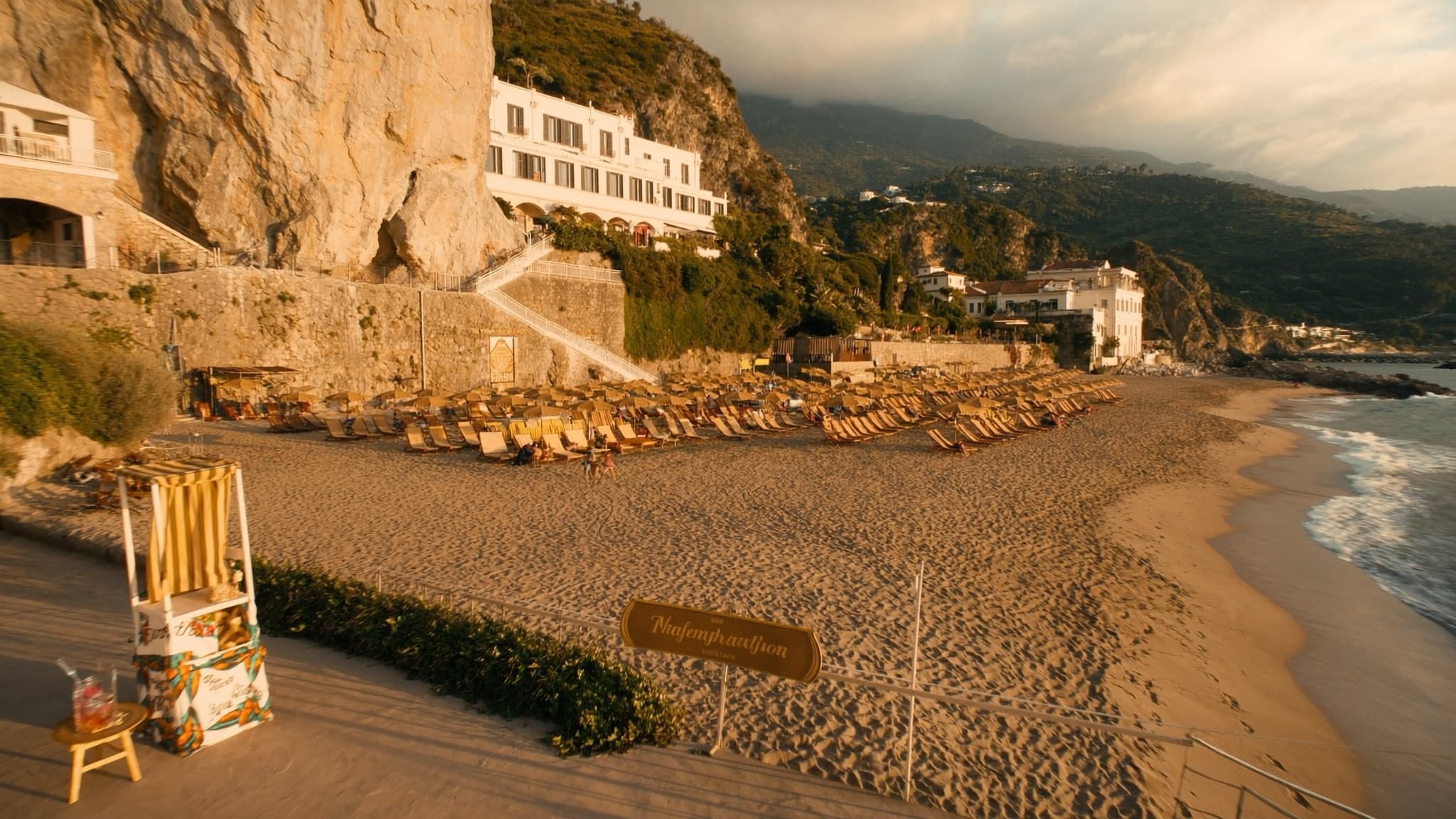 Wide establishing shot of a cliffside Amalfi coast beach club at golden hour